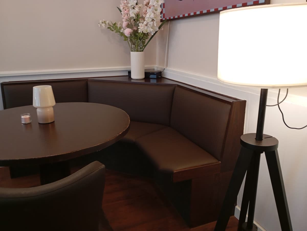 Neu bezogene Eckbank in braunem Kunstleder mit rundem Tisch und Stehlampe