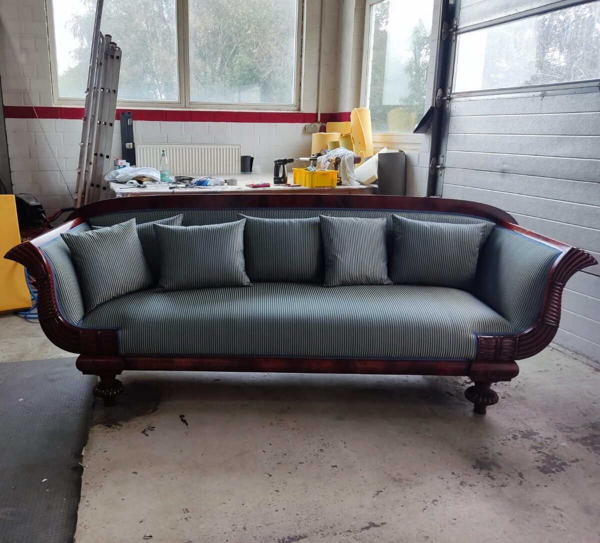 Biedermeier-Sofa mit neu bezogenem blau-grün gestreiftem Stoff und passenden Kissen in der Polsterwerkstatt