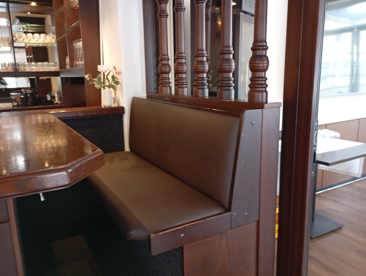 Lange neu bezogene Sitzbank in braunem Kunstleder neben der Theke eines Restaurants